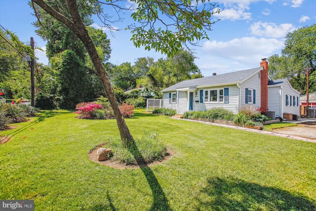 view of front of property with a front yard, central AC unit, a chimney, and roof with shingles