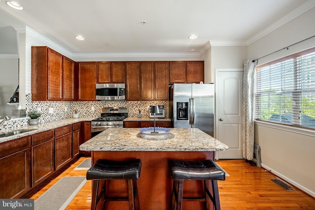 kitchen featuring stainless steel appliances, a sink, a kitchen bar, light wood finished floors, and backsplash