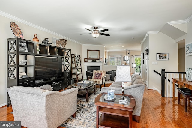 living room featuring ceiling fan, hardwood / wood-style floors, ornamental molding, baseboards, and a fireplace