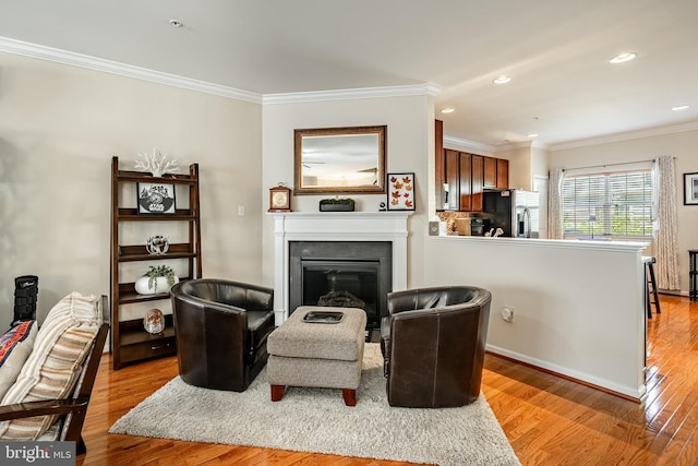 living area with crown molding, light wood finished floors, a glass covered fireplace, recessed lighting, and baseboards