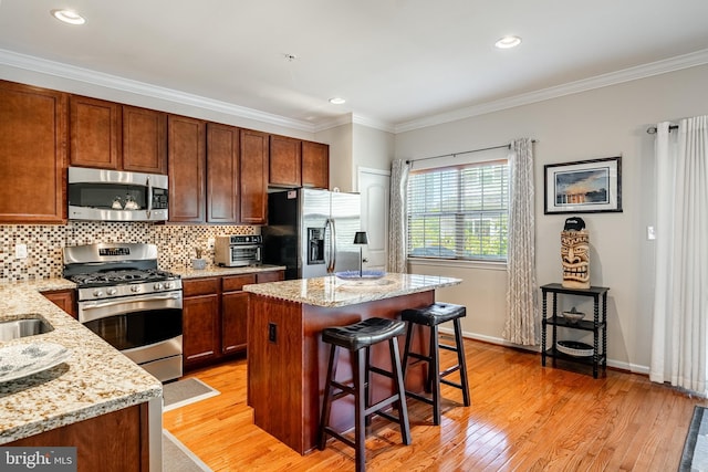 kitchen with appliances with stainless steel finishes, light wood finished floors, backsplash, a kitchen island, and light stone countertops
