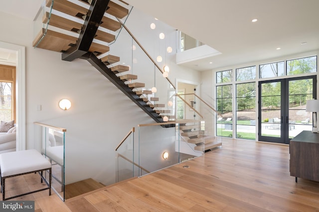 stairway featuring a high ceiling, french doors, a healthy amount of sunlight, and wood finished floors