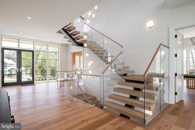 stairway featuring recessed lighting, french doors, a towering ceiling, and wood finished floors
