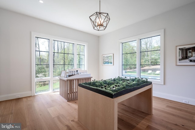 interior space with light wood-type flooring, a center island, a notable chandelier, hanging light fixtures, and baseboards
