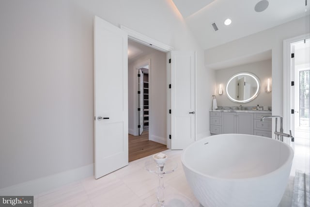 bathroom with baseboards, visible vents, vanity, a soaking tub, and vaulted ceiling