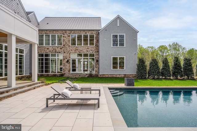 rear view of property featuring a lawn, a patio area, and an outdoor pool