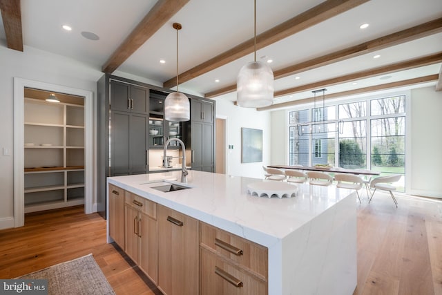 kitchen featuring a sink, a large island, light wood-style flooring, beamed ceiling, and light stone countertops