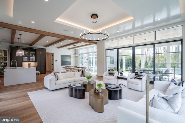living room featuring a notable chandelier, a tray ceiling, recessed lighting, beamed ceiling, and light wood-style floors