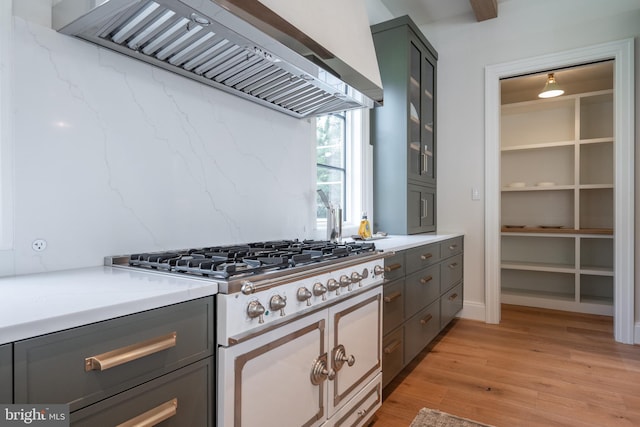 kitchen featuring glass insert cabinets, light wood finished floors, custom range hood, light countertops, and gray cabinets