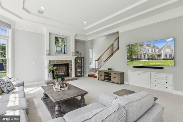 carpeted living area featuring a raised ceiling, stairs, a stone fireplace, and recessed lighting