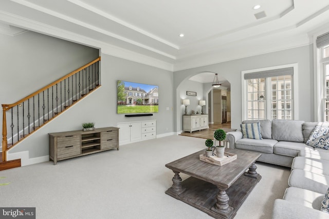 living room featuring a tray ceiling, stairway, arched walkways, and carpet floors