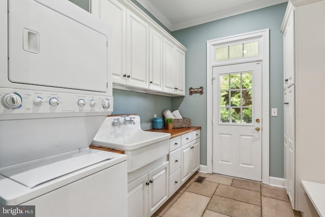 washroom featuring stacked washer / dryer, a sink, cabinet space, crown molding, and baseboards