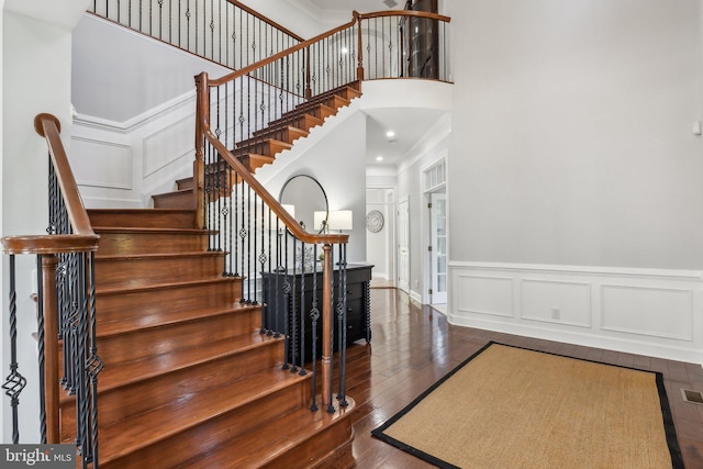 stairway featuring wood-type flooring, a high ceiling, a decorative wall, wainscoting, and ornamental molding