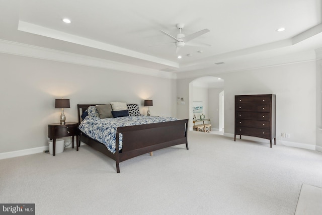 bedroom with a tray ceiling, light colored carpet, arched walkways, and recessed lighting