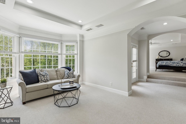 living area with a tray ceiling, carpet, and arched walkways