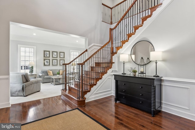 staircase featuring a high ceiling, wainscoting, hardwood / wood-style floors, and recessed lighting