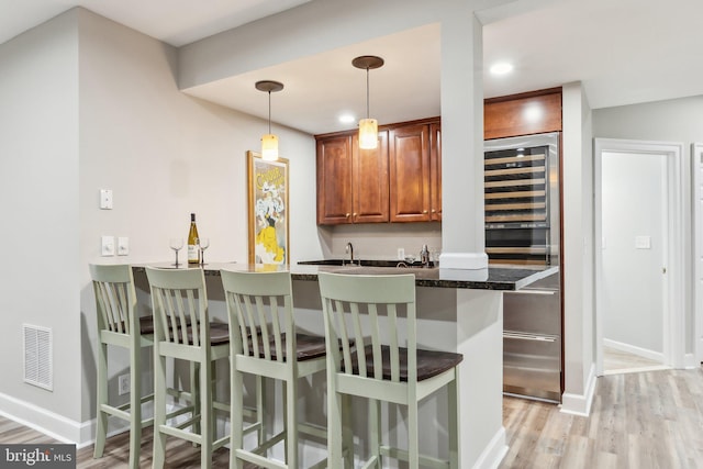 bar with pendant lighting, light wood-style flooring, baseboards, visible vents, and indoor wet bar