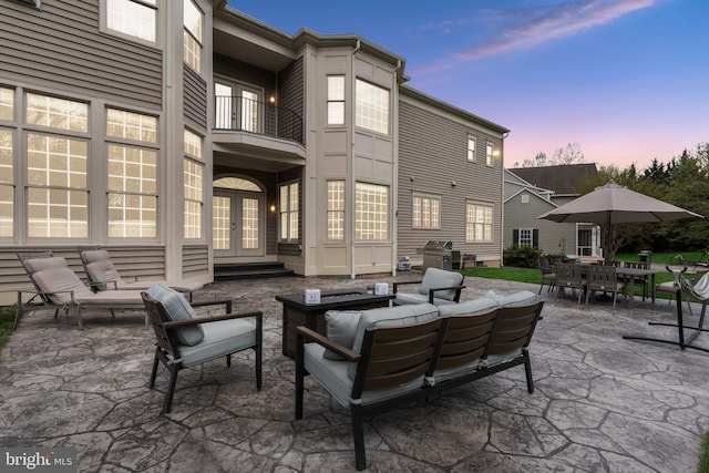 patio terrace at dusk featuring a grill, french doors, outdoor dining space, a balcony, and an outdoor hangout area