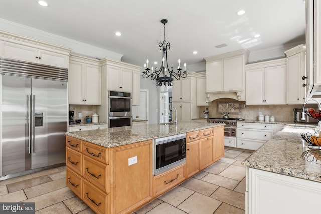 kitchen featuring crown molding, built in appliances, an island with sink, and backsplash