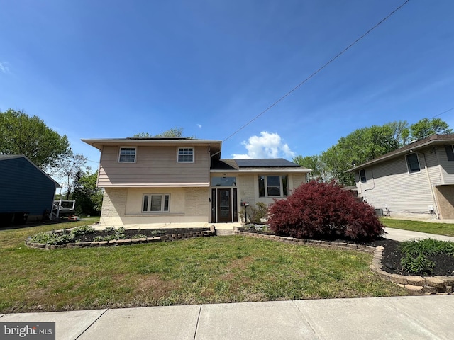 split level home featuring stucco siding, solar panels, and a front yard