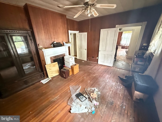 living area featuring a ceiling fan, hardwood / wood-style floors, wooden walls, and a fireplace