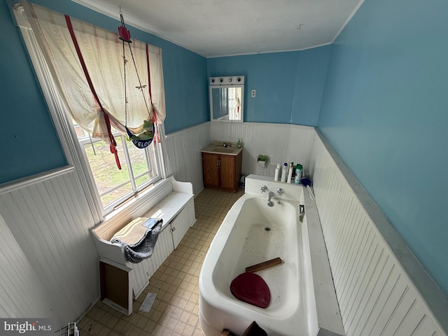 bathroom with vanity, a bathing tub, wainscoting, and a healthy amount of sunlight