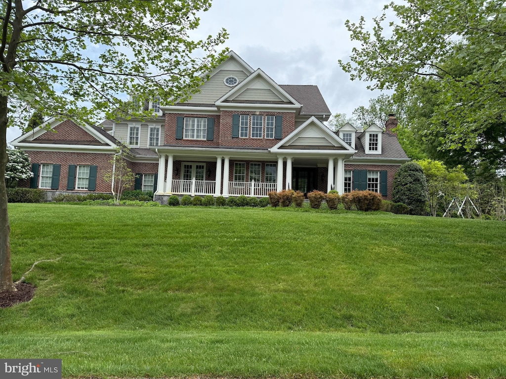 craftsman-style home featuring a chimney, a front yard, brick siding, and covered porch