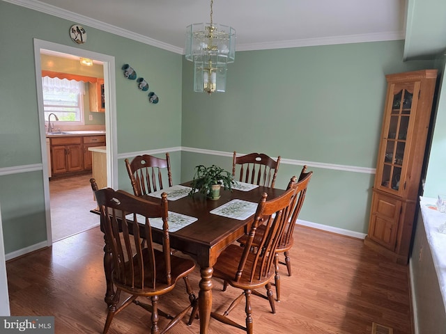 dining space featuring crown molding, light wood-type flooring, baseboards, and a notable chandelier
