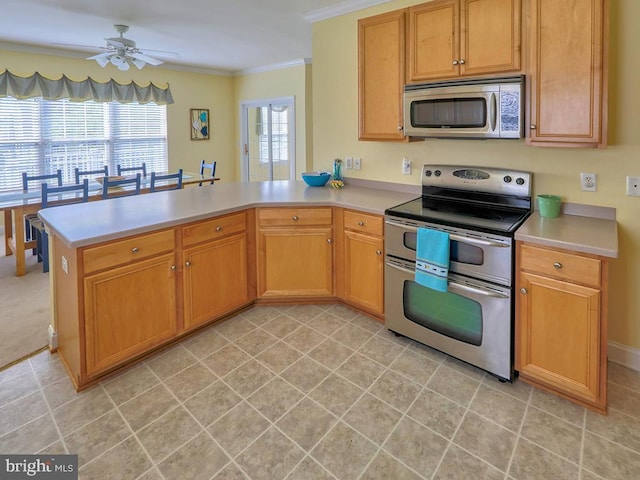 kitchen with a peninsula, stainless steel appliances, crown molding, light countertops, and a ceiling fan