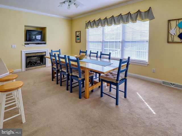 carpeted dining room featuring baseboards, ornamental molding, a glass covered fireplace, and plenty of natural light