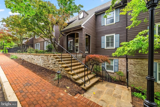 view of front of home featuring a shingled roof, brick siding, and stairway