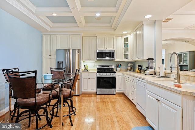 kitchen with a sink, appliances with stainless steel finishes, crown molding, arched walkways, and light wood-style floors