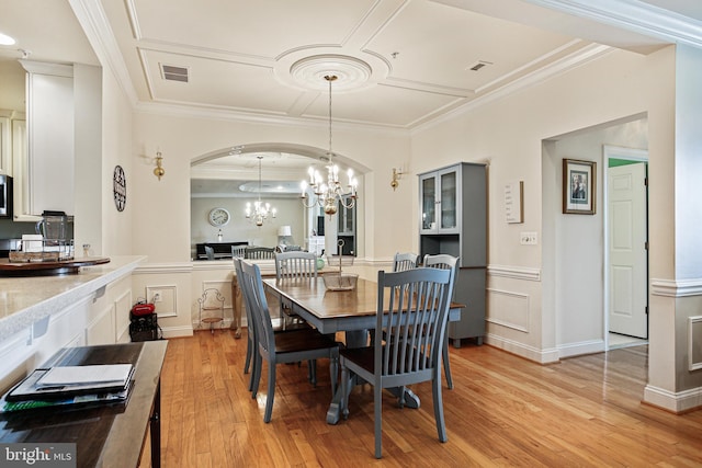 dining space featuring light wood-style flooring, an inviting chandelier, visible vents, crown molding, and arched walkways