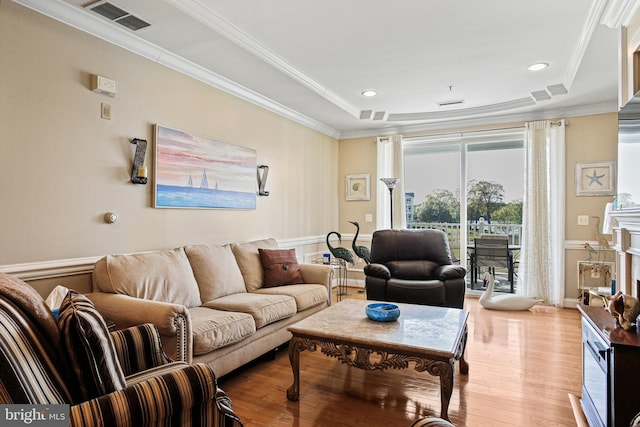 living room featuring a tray ceiling, crown molding, visible vents, and light wood-style floors