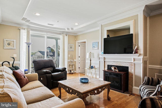 living room featuring a fireplace, crown molding, light wood-style flooring, and visible vents