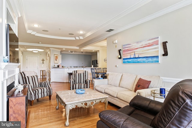 living room with a tray ceiling, a fireplace, crown molding, visible vents, and light wood-style floors
