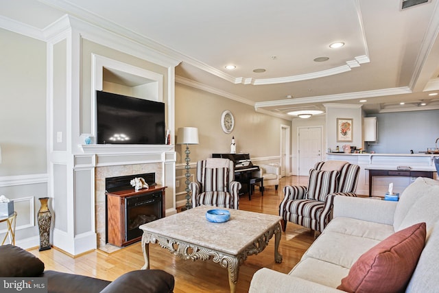 living room with light wood-style flooring, ornamental molding, a decorative wall, a wainscoted wall, and a fireplace