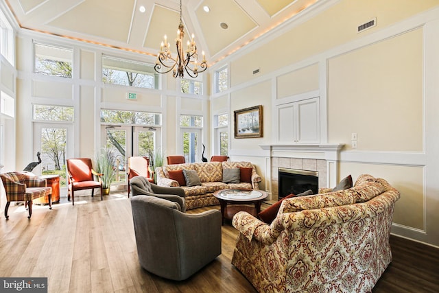living room featuring wood finished floors, visible vents, an inviting chandelier, a high ceiling, and a tile fireplace