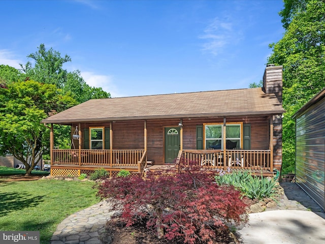 chalet / cabin with a porch, a front lawn, a chimney, and a shingled roof