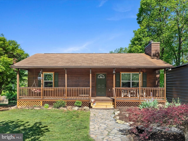 rustic home with covered porch, a chimney, a front lawn, and a shingled roof