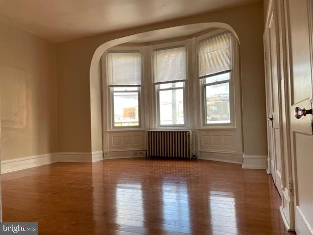spare room with wood finished floors, baseboards, arched walkways, and radiator heating unit