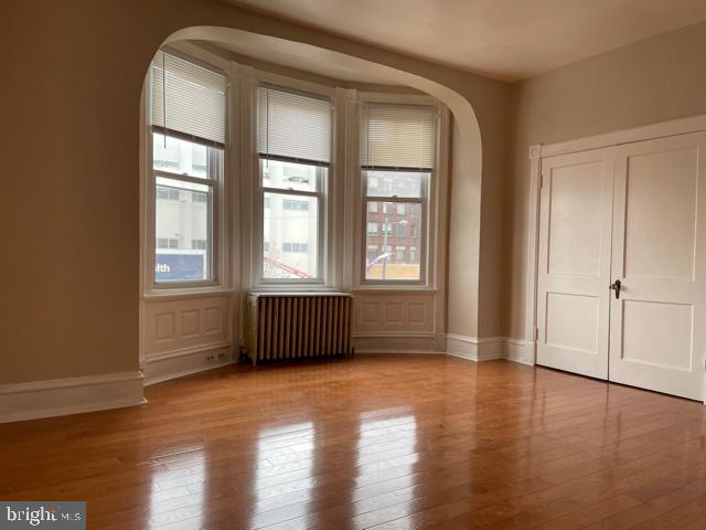 unfurnished room featuring radiator, arched walkways, baseboards, and wood finished floors