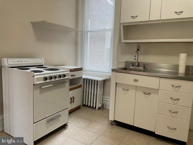 kitchen featuring radiator heating unit, a sink, stainless steel counters, white range with electric cooktop, and white cabinets