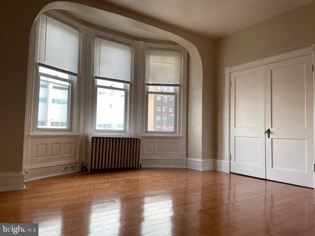 unfurnished room featuring hardwood / wood-style flooring, arched walkways, a healthy amount of sunlight, and radiator heating unit