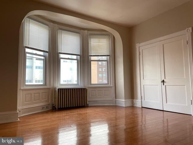 unfurnished room with wood finished floors, baseboards, arched walkways, and radiator heating unit