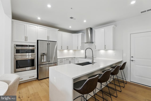 4140 Legato Rd Unit 47, Fairfax, VA 22033 - kitchen featuring stainless steel appliances, wall chimney exhaust hood, a kitchen breakfast bar, white cabinets, and light wood finished floors
