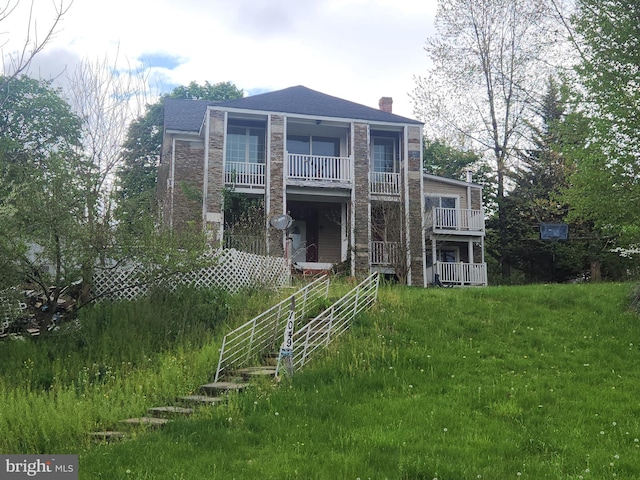 view of front facade featuring stone siding, a front lawn, a chimney, and a balcony
