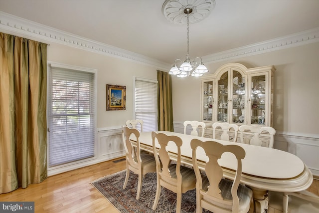 dining area featuring a chandelier, wainscoting, crown molding, a decorative wall, and light wood-style flooring