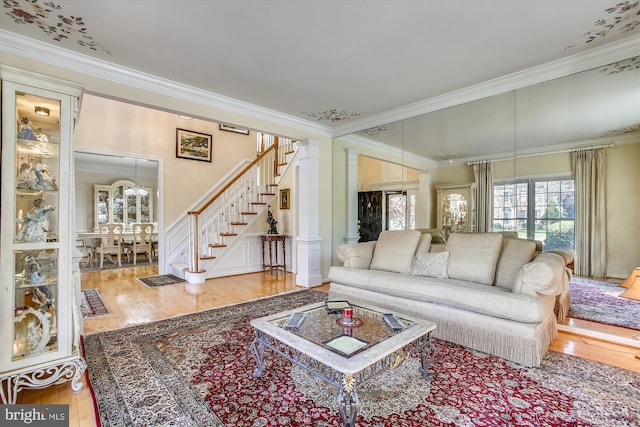 living room with ornamental molding, wood finished floors, stairs, ornate columns, and a decorative wall