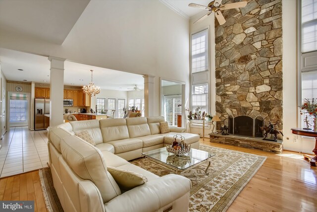 living area featuring ornate columns, ceiling fan, light wood-type flooring, crown molding, and a towering ceiling